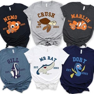 May include: Six short-sleeve t-shirts featuring characters from the movie Finding Nemo. Each shirt displays a character name, the text EST. 2003, and a graphic of Nemo, Crush, Marlin, Gill, Mr. Ray, or Dory in various colors including black, gray, blue, and white.