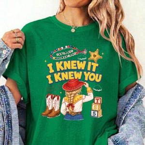 May include: A green t-shirt featuring a graphic print with the text I KNEW IT I KNEW YOU, a beaded necklace, a yellow star, a person with blonde hair wearing a red cowboy hat, two brown cowboy boots, and three stacked blocks labeled T, S, 5.