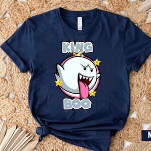 Op de afbeelding: Een marineblauw t-shirt met een afbeelding van King Boo uit de Super Mario-franchise. De afbeelding toont King Boo met een kroon en omringd door sterren. De tekst "King Boo" is onder de afbeelding gedrukt.