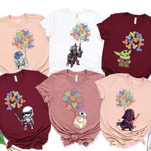 May include: A collection of six short-sleeved t-shirts in various colors, each featuring a cartoon character holding a bunch of colorful balloons. Characters include R2-D2, The Mandalorian, Baby Yoda, a Stormtrooper, BB-8, and Darth Vader.