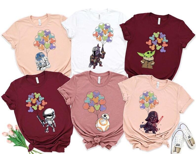 May include: A collection of six short-sleeved t-shirts in various colors, each featuring a cartoon character holding a bunch of colorful balloons. Characters include R2-D2, The Mandalorian, Baby Yoda, a Stormtrooper, BB-8, and Darth Vader.
