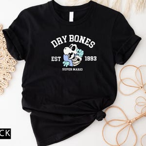 May include: Black t-shirt with a white graphic of a skeleton wearing a blue cap and holding a bone. The graphic says "Dry Bones Est 1993 Super Mario".