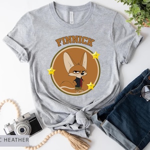 May include: Athletic heather gray t-shirt featuring a cartoon image of Finnick from Zootopia. The design includes Finnick's image inside a brown circle with the name "Finnick" above and yellow stars on each side.