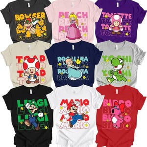 May include: A collection of nine short-sleeved t-shirts featuring various Nintendo characters including Bowser, Peach, Toadette, Toad, Rosalina, Yoshi, Luigi, Mario, and Birdo. Each shirt displays the character's name in a repeating block pattern.