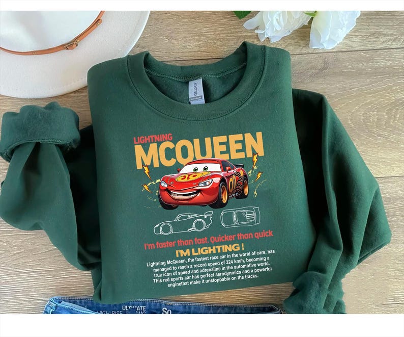 May include: A dark green sweatshirt featuring Lightning McQueen, a red race car from the Cars movie. The design includes the text "LIGHTNING MCQUEEN" and "I'm faster than fast. Quicker than quick. I'M LIGHTING!"