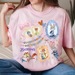 Puede incluir: Camiseta rosa claro con personajes de Zootopia y la palabra "Zootopia". El dise&ntilde;o incluye retratos enmarcados de Judy Hopps y Nick Wilde, junto con otros personajes y elementos decorativos. La camiseta es de color rosa claro.