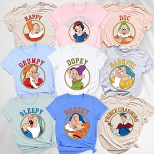 Può includere: Una collezione di nove magliette a maniche corte in vari colori pastello, ognuna con una grafica circolare di un personaggio di Biancaneve con il nome stampato sopra in un carattere arcuato, tra cui Happy, Snow White, Doc, Grumpy, Dopey, Bashful, Sleepy, Sneezy e Prince Charming.