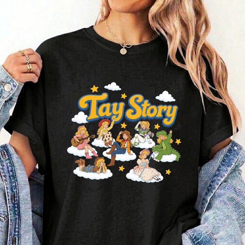 Pu&ograve; includere: Una t-shirt nera con il testo giallo Tay Story sopra un'illustrazione grafica di diversi personaggi dei cartoni animati con capelli biondi, ognuno seduto su nuvole bianche circondate da piccole stelle gialle su uno sfondo scuro.