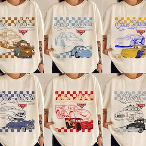 May include: Cream-colored t-shirts featuring various characters from the movie "Cars." Designs include "Tow Mater," "Sally Carrera," "Cruz Ramirez," "Doc Hudson," "Lightning McQueen," and "Sheriff," each with the "Cars" logo and year.