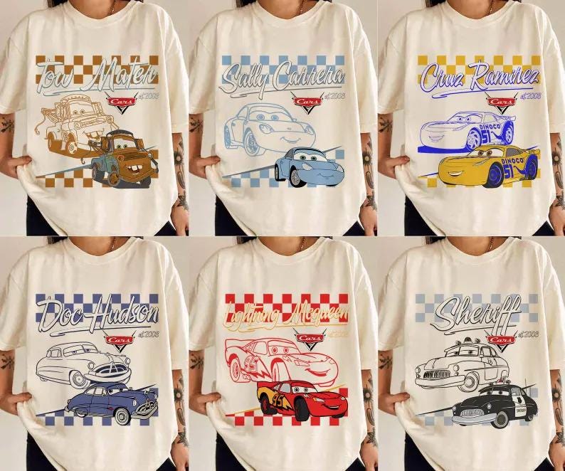 May include: Cream-colored t-shirts featuring various characters from the movie "Cars." Designs include "Tow Mater," "Sally Carrera," "Cruz Ramirez," "Doc Hudson," "Lightning McQueen," and "Sheriff," each with the "Cars" logo and year.