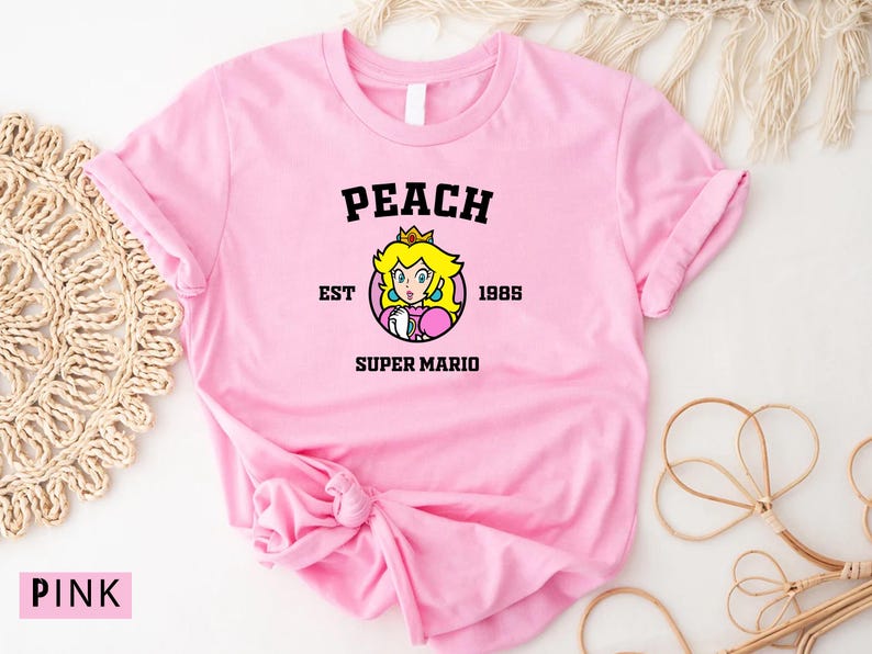 May include: Pink t-shirt with a peach character graphic and the text "Peach Est. 1985 Super Mario".