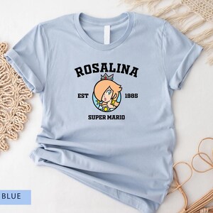 May include: Light blue t-shirt with a black graphic of Rosalina from Super Mario. The graphic includes the text "Rosalina Est 1985 Super Mario".