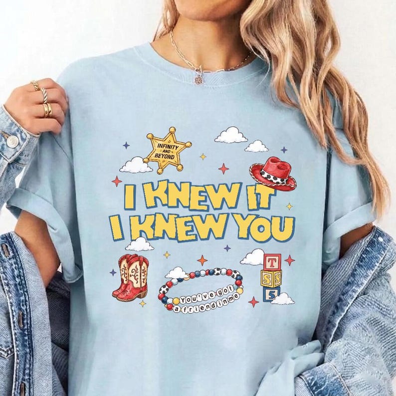 Puede incluir: Una camiseta azul claro con un estampado gr&aacute;fico que incluye el texto I KNEW IT I KNEW YOU, una estrella de sheriff amarilla, un sombrero de vaquero rojo, un par de botas vaqueras rojas, una pulsera de cuentas colorida y tres cubos.