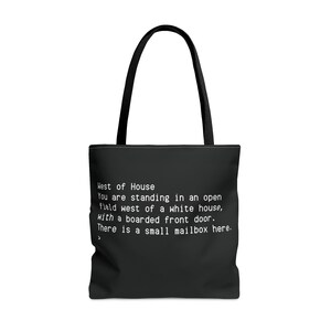 Puede incluir: Bolsa de tela negra con texto blanco que dice: "West of House You are standing in an open field west of a white house, with a boarded front door. There is a small mailbox here."