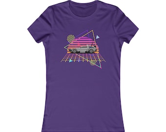 May include: Purple women's t-shirt with a retro 80s design featuring a silver car driving through a grid pattern with a sunset in the background.