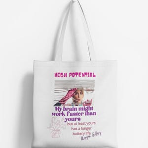 Könnte beinhalten: Weiße Einkaufstasche mit einer pinkfarbenen und violetten Grafik einer Frau, die aus einem Fenster schaut, mit dem Text "HIGH POTENTIAL" und "My brain might work faster than yours but at least yours has a longer battery life" und einer Unterschrift, die "Morgan Gilbert" lautet.