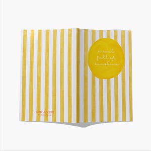 Puede incluir: Cuaderno abierto con páginas a rayas amarillas y blancas. Un círculo amarillo con las palabras "a soul full of sunshine" está en la página derecha. La esquina inferior izquierda tiene el texto "SLATE & SCRIPT Printed in the UK."