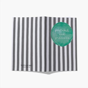 May include: Open notebook with a striped gray and white pattern. A green watercolor circle with the words "grateful and gracious" is on the right page. The text "SLATE & SCRIPT Printed in the UK" is at the bottom.