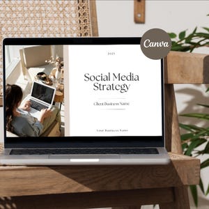 Op de afbeelding: Een laptop met een presentatie "Social Media Strategy", met het Canva-logo. De laptop staat op een houten stoel. Een persoon werkt op de laptop. De achtergrond omvat een raam en een plant.