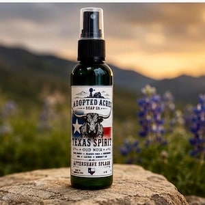May include: A dark green spray bottle of Adopted Acres Soap Co. Texas Spirit Oud Noir aftershave splash. The label features a longhorn steer illustration, a Texas flag graphic, and the text 4 oz. The bottle has a black pump sprayer top.