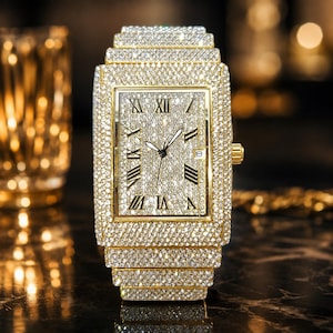 May include: A rectangular gold-tone wristwatch featuring a dial and case fully encrusted with clear, sparkling stones. The watch face displays black Roman numeral hour markers, thin black hands, and a small date window at the three o'clock position.