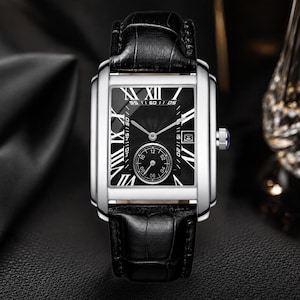 May include: A rectangular wristwatch with a polished silver-tone case and a black textured leather strap. The black dial features white Roman numeral hour markers, silver hands, a small seconds sub-dial at the bottom, and a date window at the three o'clock position.