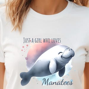 Puede incluir: Camiseta blanca con un diseño de acuarela de un manatí y el texto "Just a girl who loves manatees".