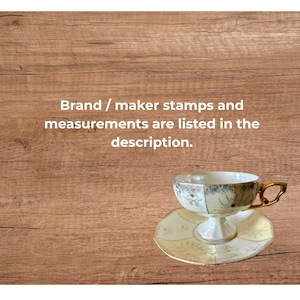 May include: A vintage teacup and saucer set. The teacup is white with gold trim and floral accents. The saucer is a matching design. The set is on a wooden surface. Text in the image reads: Brand / maker stamps and measurements are listed in the description.