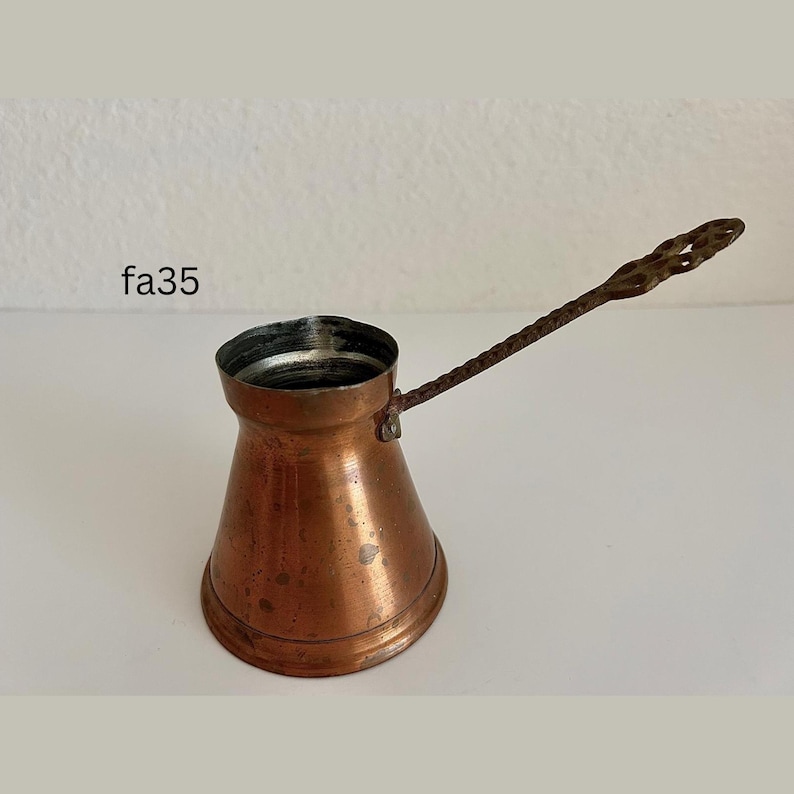 May include: A copper-colored Turkish coffee pot with a long, twisted handle. The pot has a wide base that tapers to a narrow neck and a flared rim. The handle is attached to the side of the pot. The text "fa35" is visible in the image.