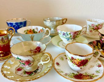 May include: A collection of assorted porcelain teacups and saucers featuring various floral patterns, gold-trimmed edges, and intricate designs. The set includes cups with red, yellow, and pink rose motifs, blue patterns, and scalloped rims.
