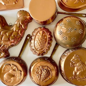 May include: An assortment of vintage copper kitchenware, including molds and pans. The collection features a rooster, pineapple, and squirrel design. The pans have brass handles and are in various sizes.