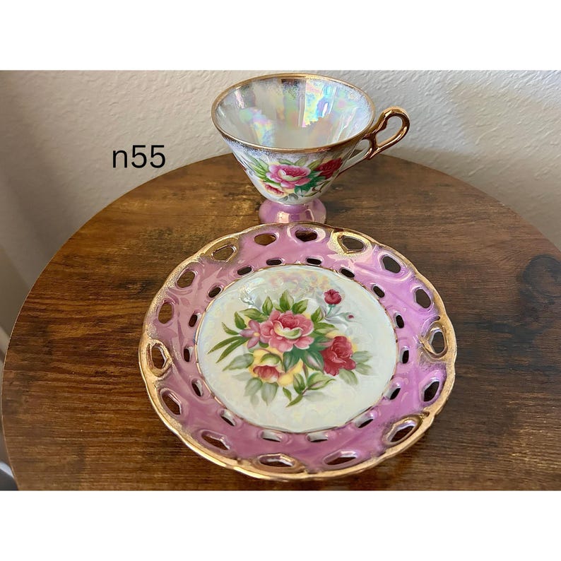 May include: A vintage teacup and saucer set. The iridescent teacup has a gold handle and is decorated with pink roses. The pink saucer has a gold trim and a floral center design. The text "n55" is visible on the left.