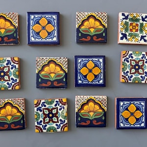 May include: A collection of twelve square ceramic tiles with colorful floral designs. The tiles feature yellow, blue, green, and red patterns on a dark blue background. Each tile is approximately 4 inches square.