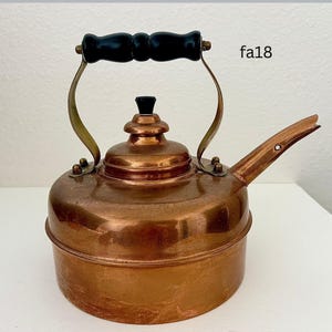 May include: A vintage copper tea kettle with a black wooden handle and spout. The kettle has brass accents and a small black knob on the lid. The text "fa18" is visible on the side of the kettle.