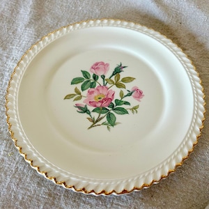 May include: A white ceramic plate with a gold rim and a floral design featuring pink roses and green leaves.