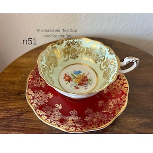 May include: A mismatched tea cup and saucer set. The cup is light green with gold filigree and a floral center. The saucer is red with gold filigree. The text "Mismatched Tea Cup and Saucer Set" and "n51" are visible.