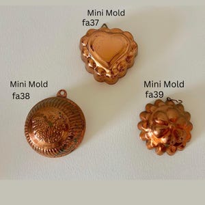 May include: Three antique copper mini molds. The molds are in the shapes of a heart, a flower, and a round design. Each mold has a small loop for hanging. The text "Mini Mold" and a catalog number are printed on the image.