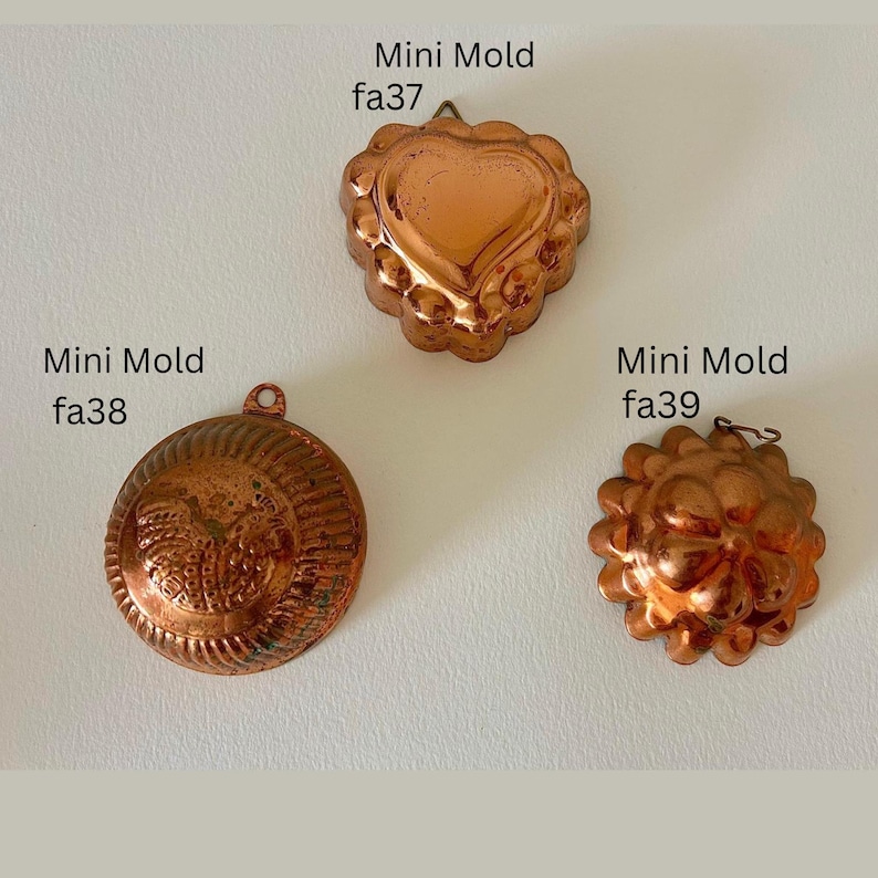 May include: Three antique copper mini molds. The molds are in the shapes of a heart, a flower, and a round design. Each mold has a small loop for hanging. The text "Mini Mold" and a catalog number are printed on the image.