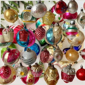 May include: A collection of vintage glass Christmas ornaments in various shapes and colors, including spheres, pinecones, and basket designs. The ornaments feature metallic, glossy, and matte finishes with painted floral, striped, and textured details.