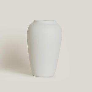 Könnte beinhalten: Eine weiße Vase mit matter Oberfläche, rundem Körper und leicht ausgestellter Öffnung. Die Vase hat ein glattes, minimalistisches Design, das sich zum Präsentieren von Blumen oder als dekoratives Element eignet. Die Vase ist etwa 25 cm hoch.
