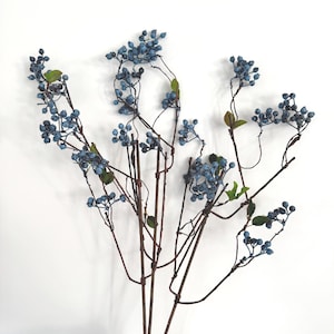Könnte beinhalten: Ein Bund künstlicher blauer Beerenstiele mit braunen Zweigen und kleinen grünen Blättern. Die Beeren sind in Büscheln angeordnet und haben eine strukturierte Oberfläche. Auf weißem Hintergrund.