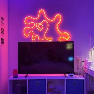 May include: A purple room with a TV and a white shelf with blue drawers. The wall behind the TV has a neon light in the shape of an abstract design.