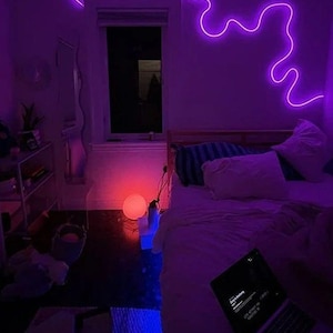 May include: A bedroom with a bed, a laptop, and a purple neon light on the wall. The room is lit with a purple and blue glow.
