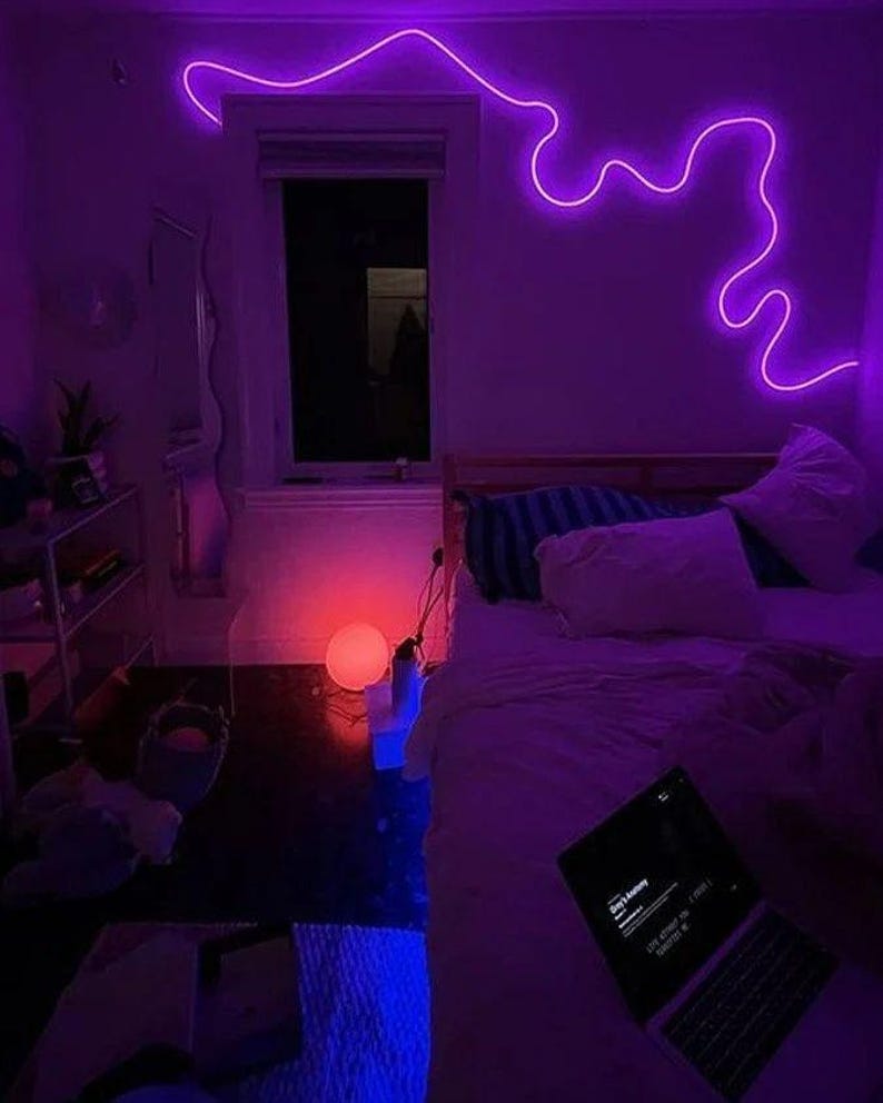 May include: A bedroom with a bed, a laptop, and a purple neon light on the wall. The room is lit with a purple and blue glow.