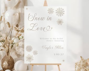 May include: A white rectangular bridal shower welcome sign on a wooden easel featuring the text Snow in Love, Welcome to the bridal shower honouring Taylor Allen, and the date 1/10/27, decorated with gold-toned snowflake illustrations.