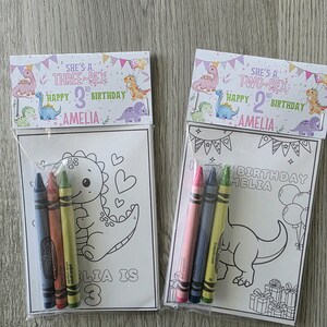 May include: Two birthday party favor bags with coloring pages and crayons. One bag says "She's a Three-Rex Happy 3rd Birthday Amelia" and the other says "She's a Two-Rex Happy 2nd Birthday Amelia". Each bag contains a coloring page and a set of crayons.