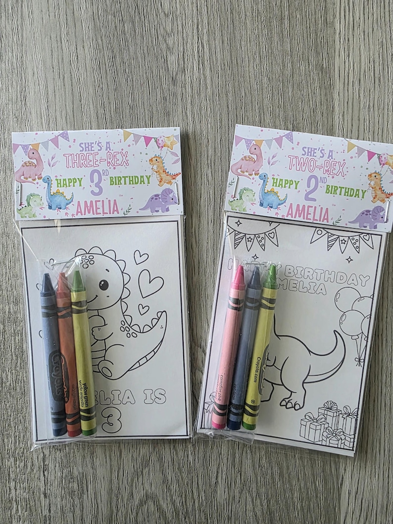 May include: Two birthday party favor bags with coloring pages and crayons. One bag says "She's a Three-Rex Happy 3rd Birthday Amelia" and the other says "She's a Two-Rex Happy 2nd Birthday Amelia". Each bag contains a coloring page and a set of crayons.