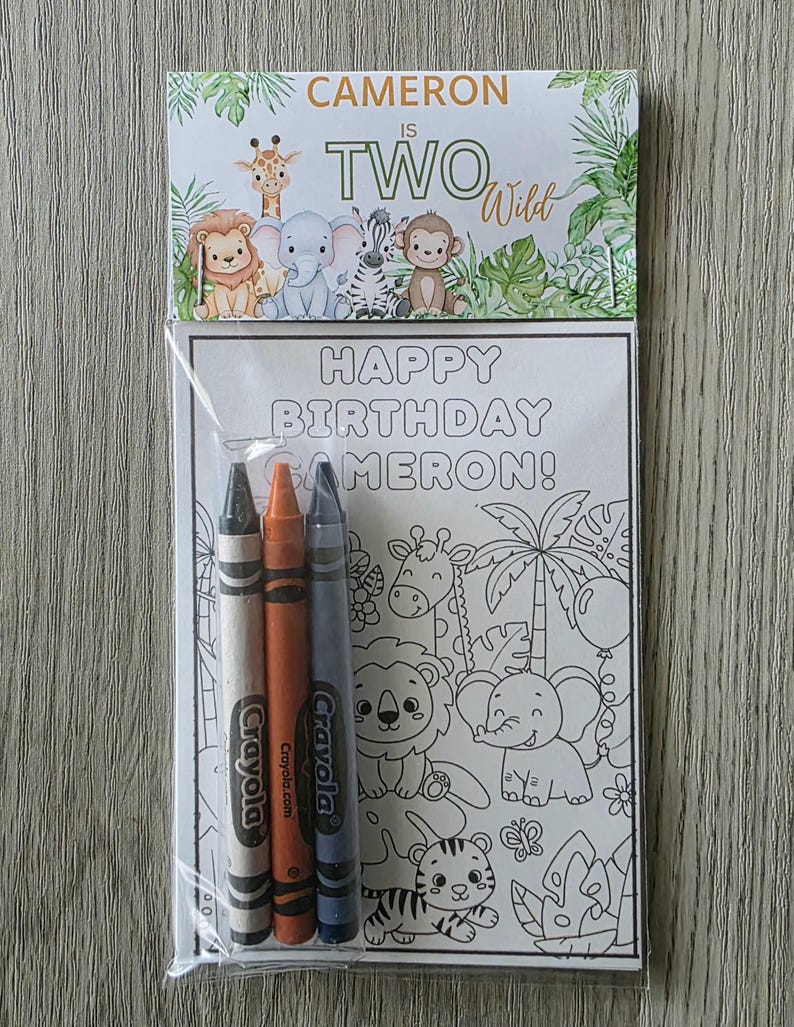 May include: A clear plastic bag contains a coloring book and three crayons. The coloring book has a jungle theme with the text "HAPPY BIRTHDAY CAMERON!" and "CAMERON IS TWO Wild". The crayons are gray, orange, and blue.
