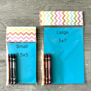 May include: Two clear plastic bags with colorful zigzag patterned tops. The smaller bag, labeled "Small 3.5x5", contains four crayons. The larger bag, labeled "Large 5x7", contains three crayons. The bags are on a wooden surface.