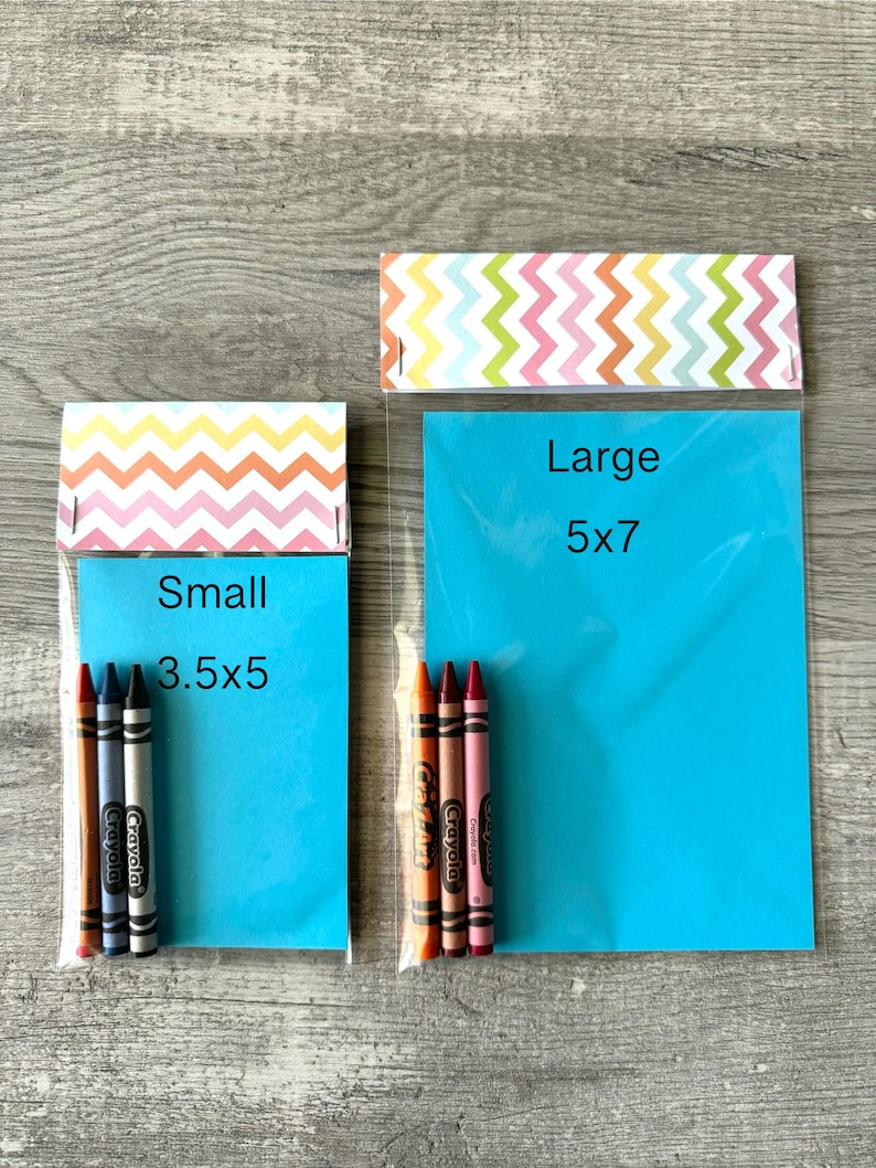 May include: Two clear plastic bags with colorful zigzag patterned tops. The smaller bag, labeled "Small 3.5x5", contains four crayons. The larger bag, labeled "Large 5x7", contains three crayons. The bags are on a wooden surface.